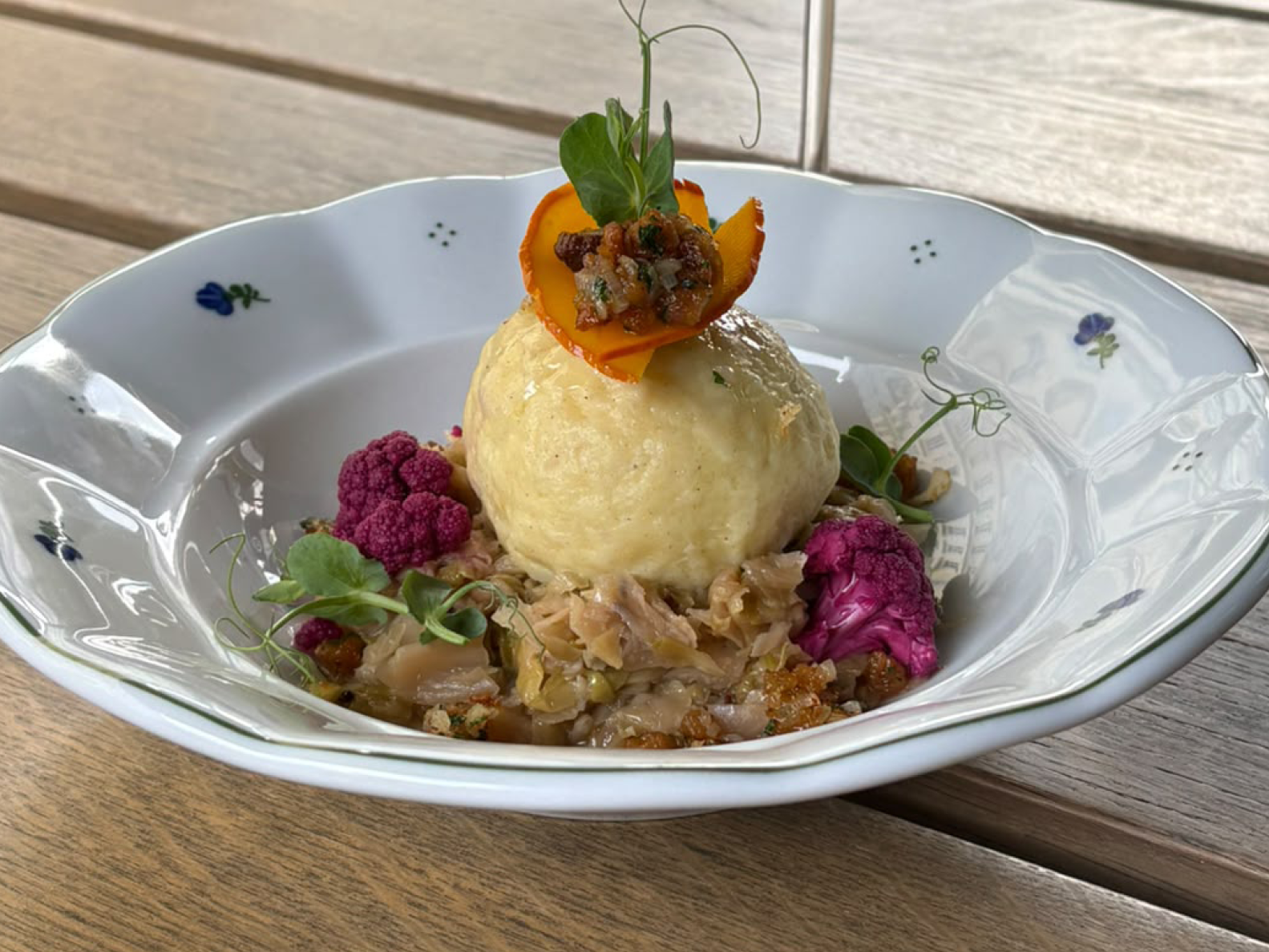 Ein großer Kartoffelknödel, serviert auf geschmortem Kohl und violettem Blumenkohl in einer dekorativen weißen Schüssel.