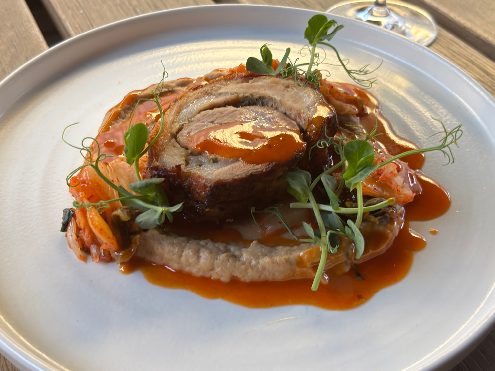 Eine Scheibe gebratener Schweinebauch, serviert auf einem Püree mit Kimchi und garniert mit Erbsensprossen.