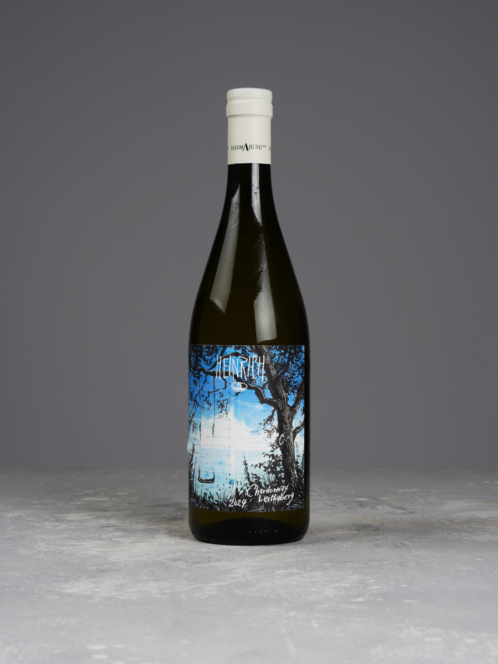 Eine Flasche Weißwein mit einem malerischen Etikett, auf dem Bäume und eine Schaukel zu sehen sind, vor einem grauen Hintergrund auf einer strukturierten Oberfläche.