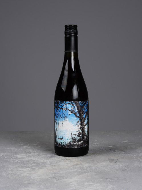 Auf einer grauen Fläche steht eine dunkle Weinflasche mit Schraubverschluss. Auf dem Etikett sind ein Baum, schwarzes Gras und ein blauer Himmel mit Wolken abgebildet, und oben steht in fetten Buchstaben das Wort „LENGTH“.
